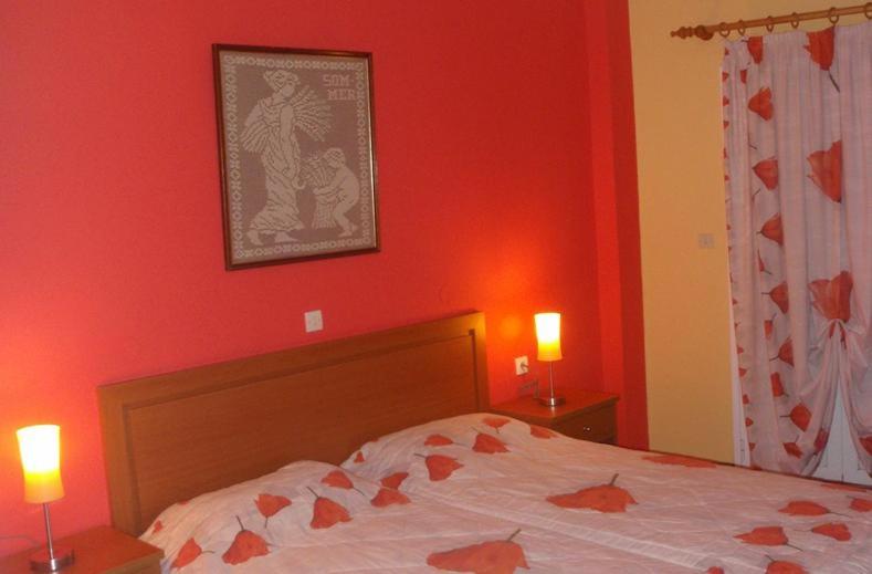 a bedroom with a bed with red walls and two lamps at Kate Apartments in Kokkari