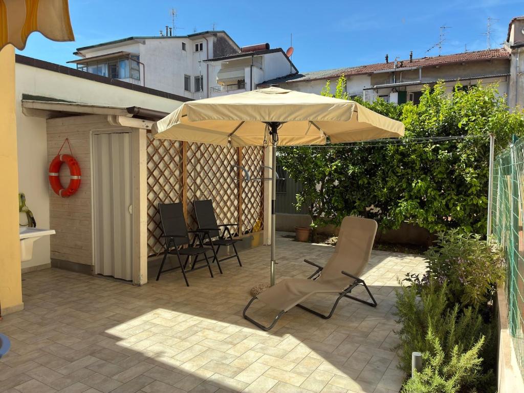 eine Terrasse mit einem Sonnenschirm, Stühlen und einem Tisch in der Unterkunft Piano terra con giardino, vicino al mare in Viareggio