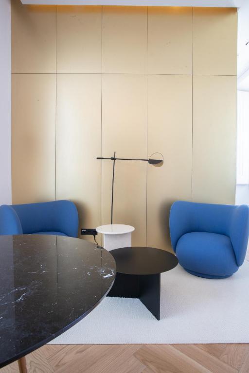 A small lounge and table setting with two blue armchairs and a wall lamp.