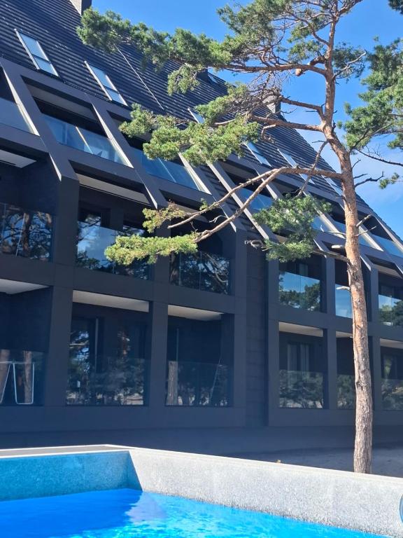 a building with a tree in front of a swimming pool at Czarna Perła 109 luksusowy apartament,basen,garaż,taras Hel in Hel