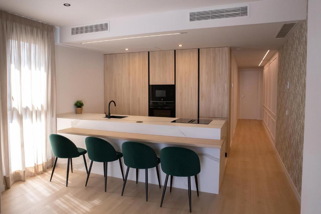 Una cocina con un mostrador con cuatro sillas verdes. en Luxury Apartament Free Parking, en Tomares