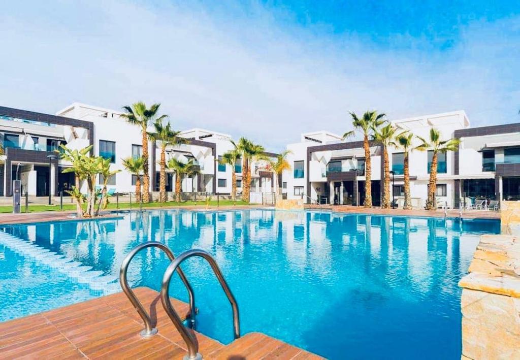 a large swimming pool with palm trees and buildings at Viva La Zenia in Orihuela Costa