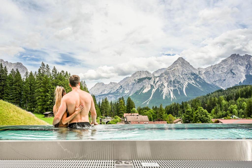 um homem e uma mulher sentados em uma piscina com montanhas em Hotel Grieserhof em Lermoos