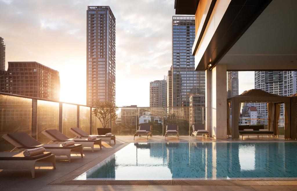 A rooftop pool deck with loungers, cabanas and a high-rise Bangkok skyline.