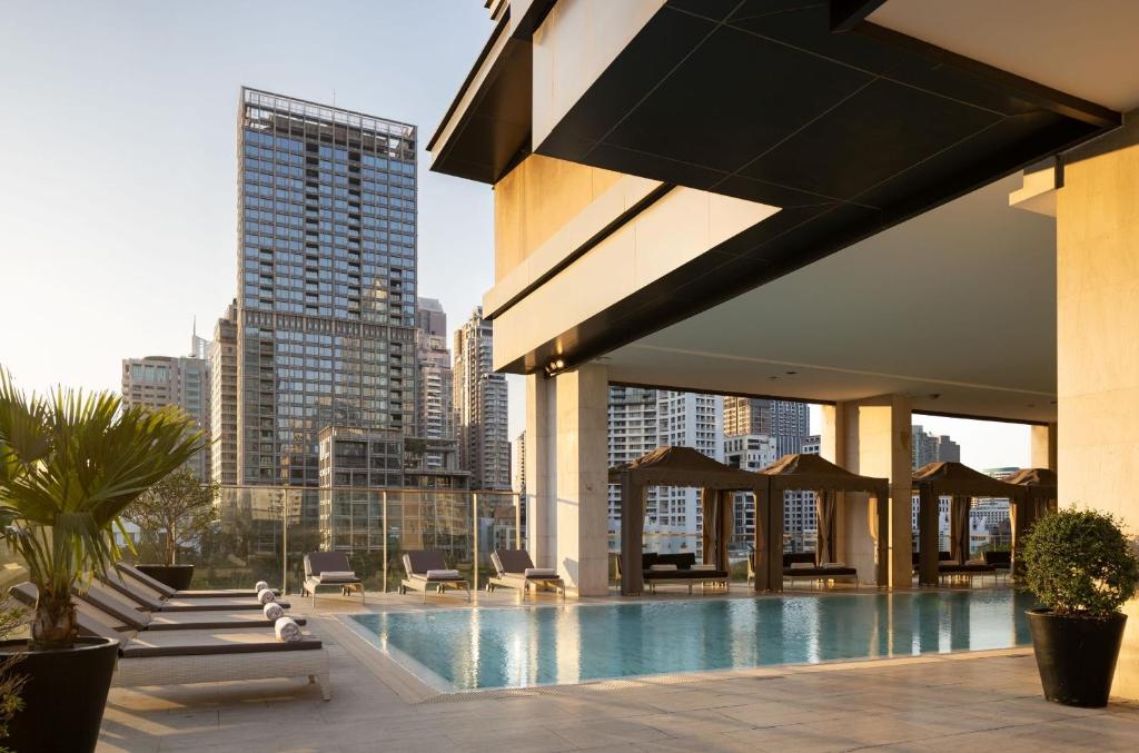 A rooftop pool terrace framed by city towers, loungers and covered cabanas.