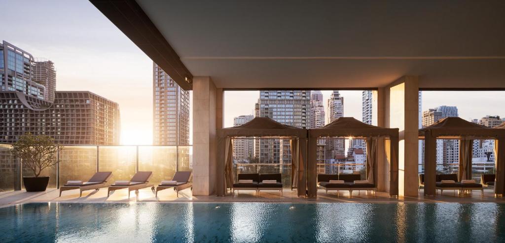 An indoor pool deck with cabanas, loungers and a sunset-lit city skyline.