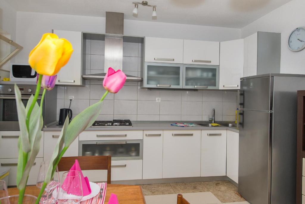 una cocina con armarios blancos y flores rosas sobre una mesa en Apartments Marieta, en Makarska