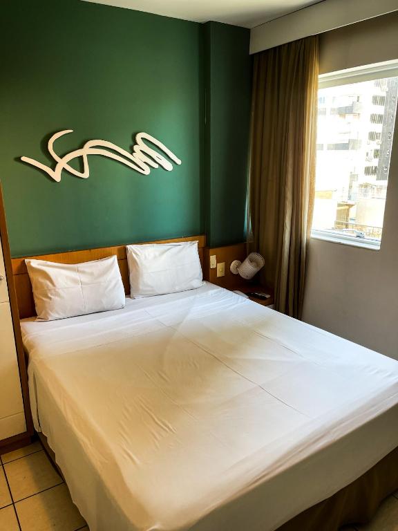 a bedroom with a large white bed with a green wall at Praia do Canto Apart Hotel - 102B in Vitória