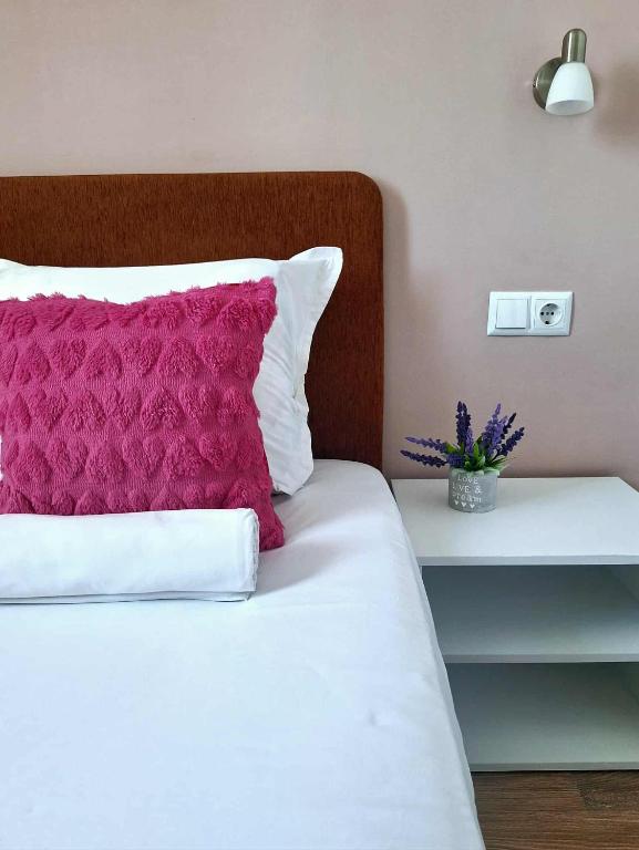 a white bed with a pink pillow and a table at Chance Sarafovo in Burgas