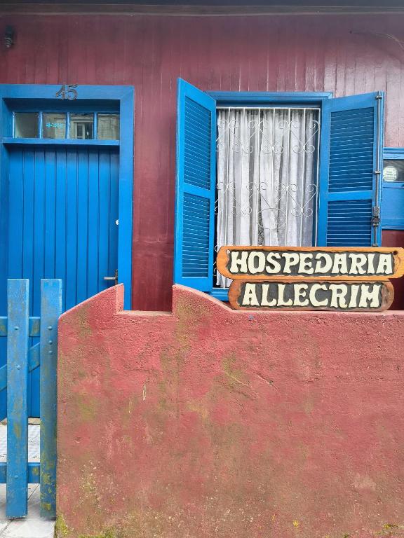 a red building with a blue door and a sign at Hospedaria Allecrim in Santo André