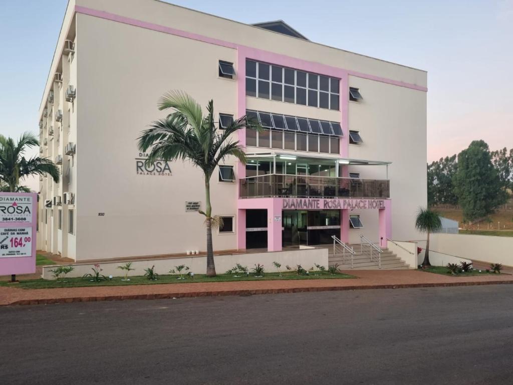 un bâtiment rose et blanc avec un palmier devant dans l'établissement Diamante Rosa Palace Hotel, à Coromandel