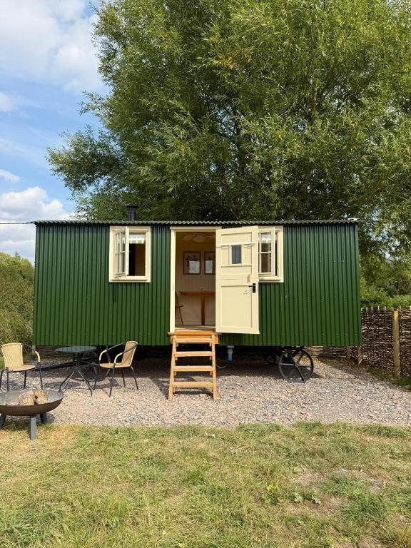a green tiny house with a ladder and chairs at Cosy Shepherd Hut in Kempsford