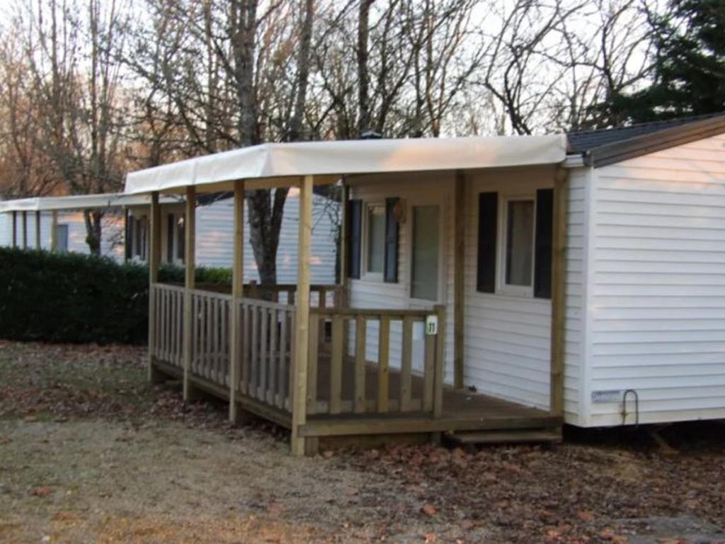 ein kleines weißes Haus mit einer Veranda an der Seite in der Unterkunft Mobil-home avec terrasse, 2 chambres, Limeuil - API-1-52-330 in Limeuil