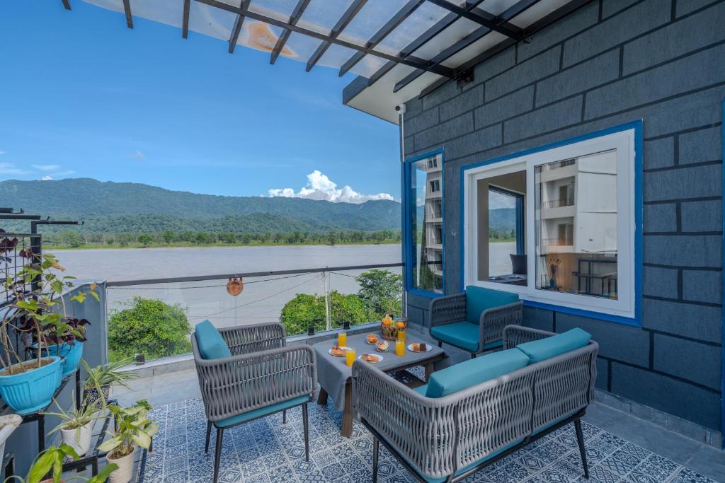 Un patio con mesa y sillas y vista al agua. en SaffronStays Tarangini by Ganges, en Rishīkesh