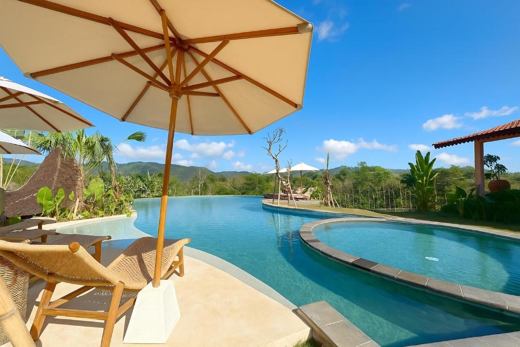 a pool at a resort with chairs and an umbrella at Tebola Joglo Villas in Sidemen