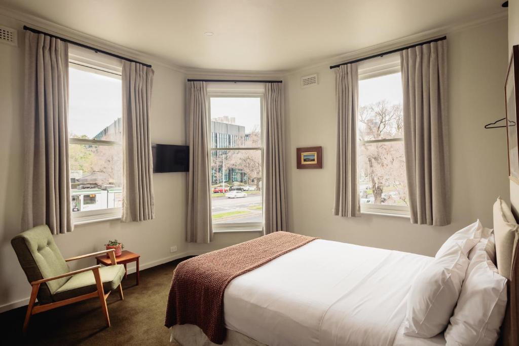 a bedroom with a bed and three windows at Naughtons Hotel in Melbourne