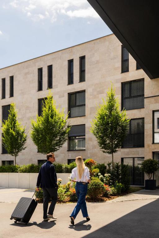 a man and a woman walking down a sidewalk with a suitcase at LMS - La Maison Suisse in Döttingen