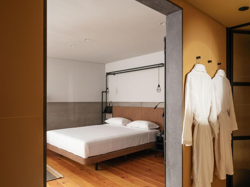 A compact double bedroom with a low bed, open hanging rail and wood flooring.