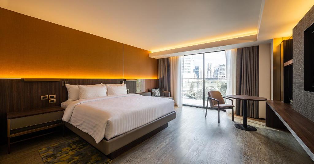 A bright hotel room pairs a king bed with a desk, lounge chair, and large window.