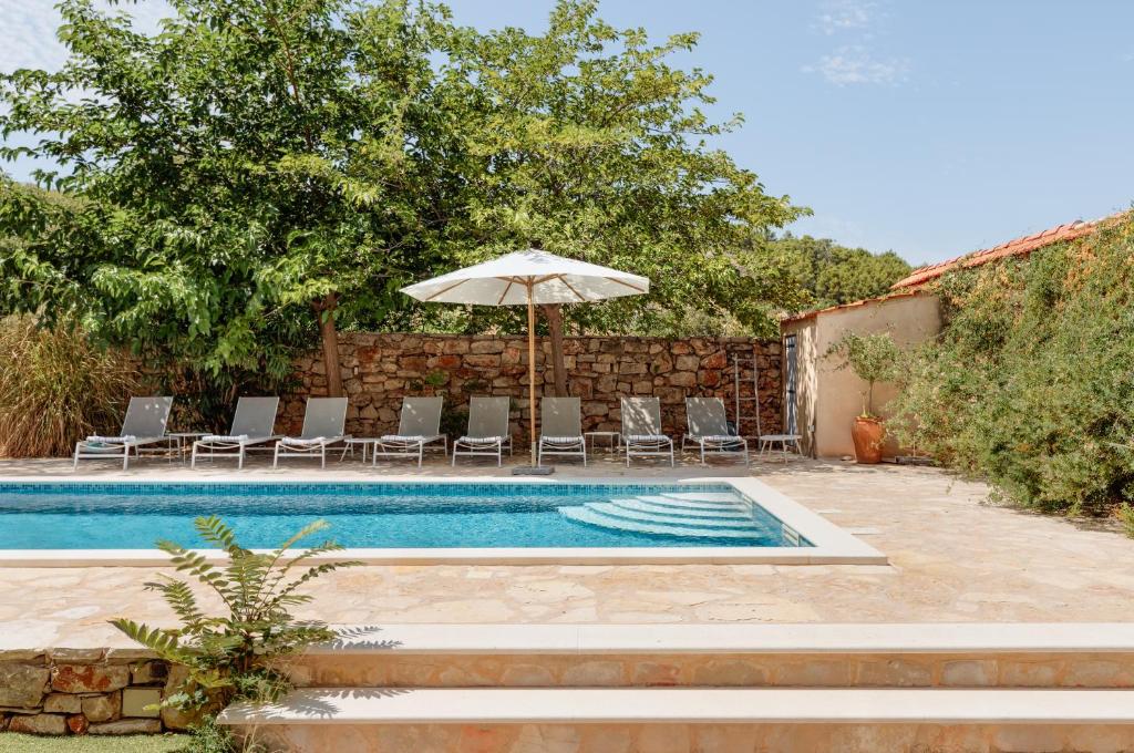 a swimming pool with an umbrella and chairs and a table and an umbrella at Villa Estelle, Hvar Island in Vrbanj