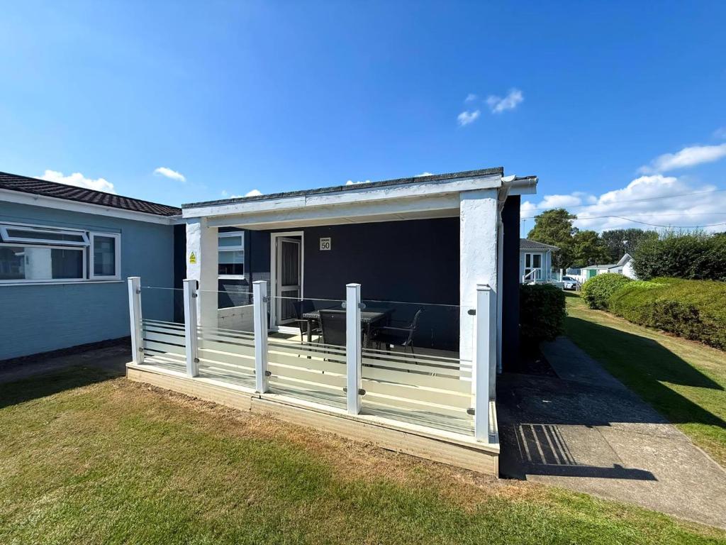 eine überdachte Veranda mit Tisch und Zaun in der Unterkunft Dog Friendly Chalet With Outdoor Seating At Broadland Park And Marina Ref 12050B in Lowestoft