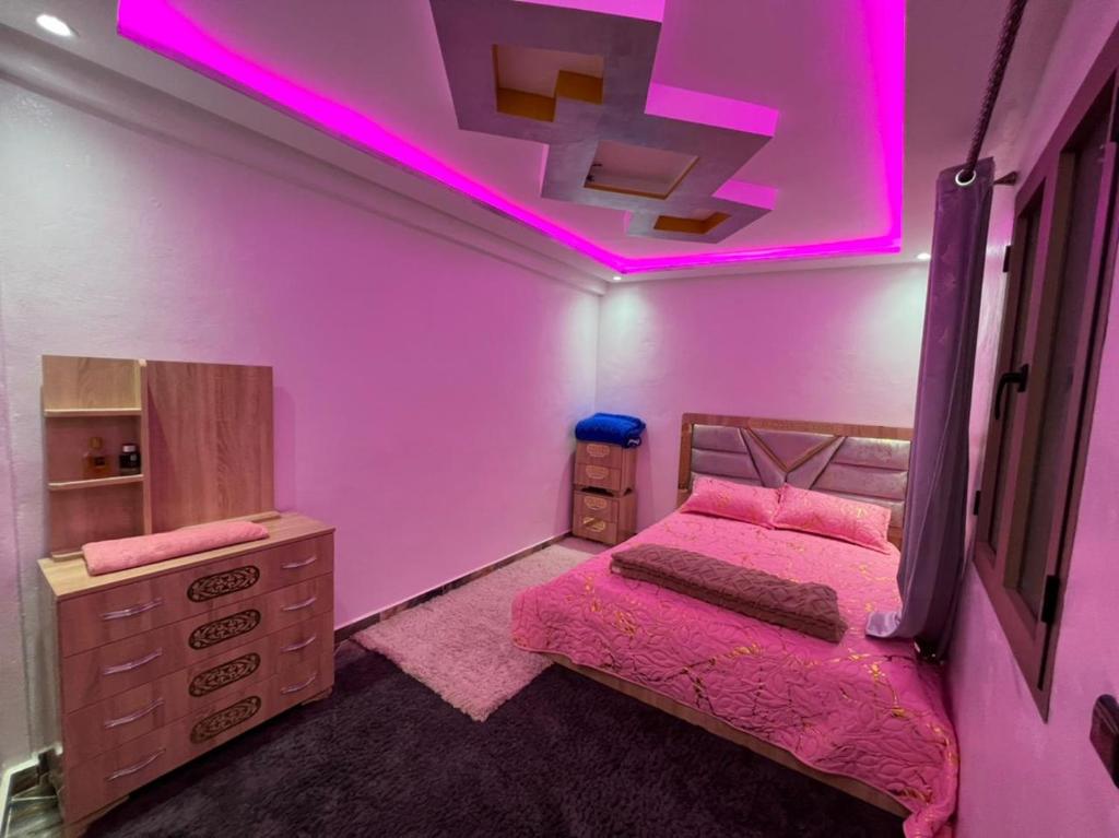 タガズートにあるBest house in taghazoutのピンクの照明、ベッド、ドレッサーが備わるベッドルーム1室が備わります。