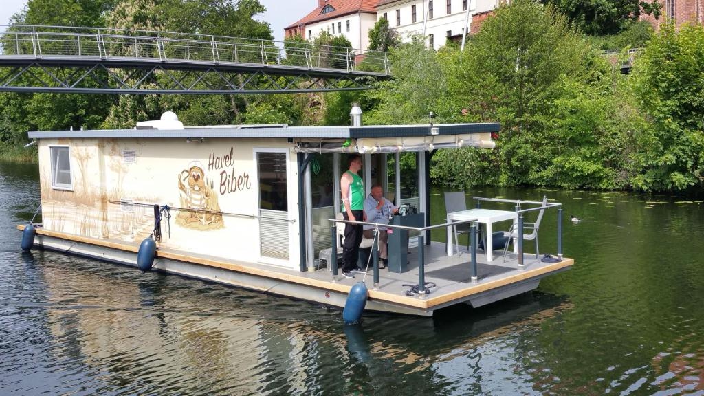 una casa galleggiante sull'acqua con due persone a bordo di Traumhaus-auf-dem-Wasser-Modernisiertes-Hausboot-13-x-4-m a Kützkow