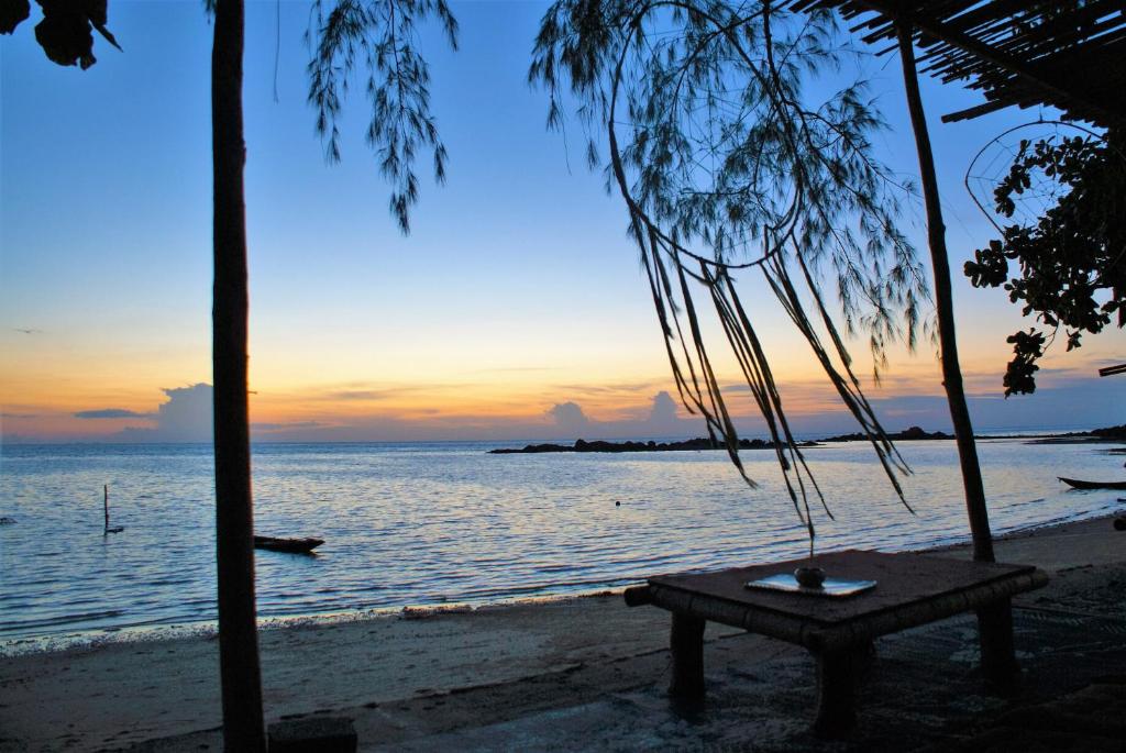 un banc sur la plage avec un coucher de soleil en arrière-plan dans l'établissement Haad Chao Phao Resort, à Haad Chao Phao