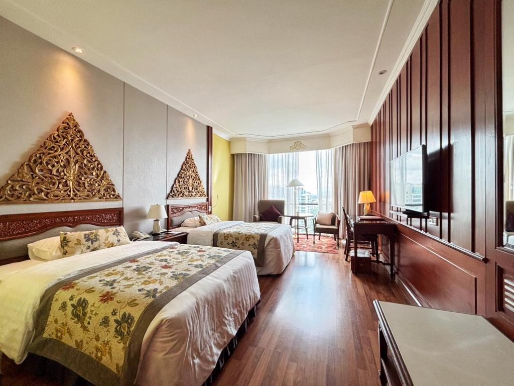 A spacious-looking twin room includes a desk, television, seating area and curtained window.