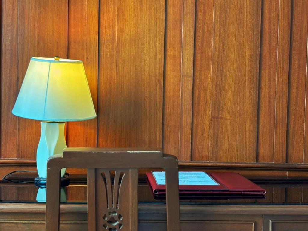 A small writing desk with a lamp, chair and hotel information folder.