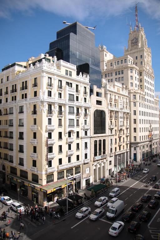 Un gran edificio blanco con coches aparcados en un estacionamiento. en Petit Palace Triball, en Madrid