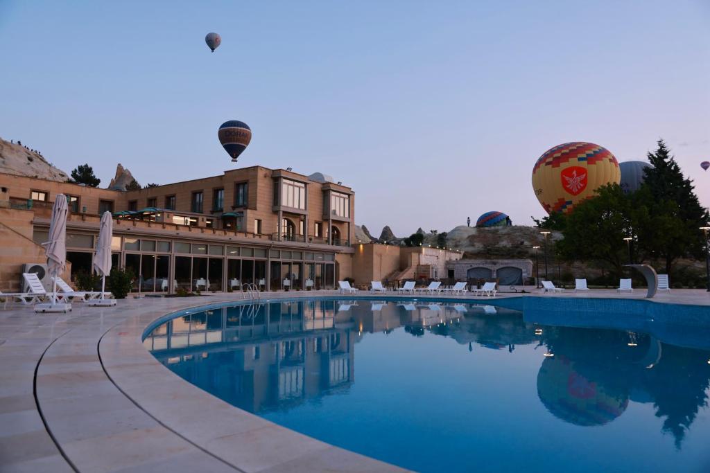 een zwembad met een gebouw en twee heteluchtballonnen bij Zemi Hotel Cappadocia in Goreme