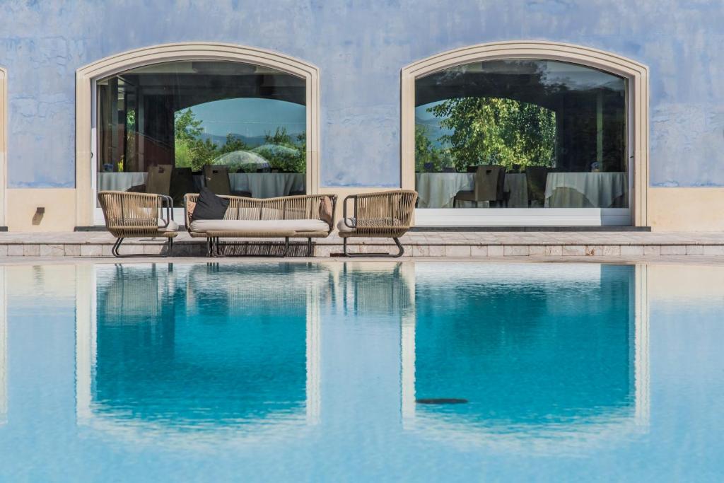 a swimming pool with chairs and a couch next to a building at Villa Neri Resort & Spa in Linguaglossa