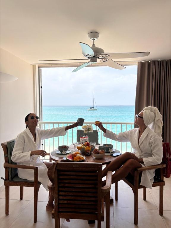 two women sitting at a table with a view of the ocean at Grand Case Beachfront Apartment in Grand Case