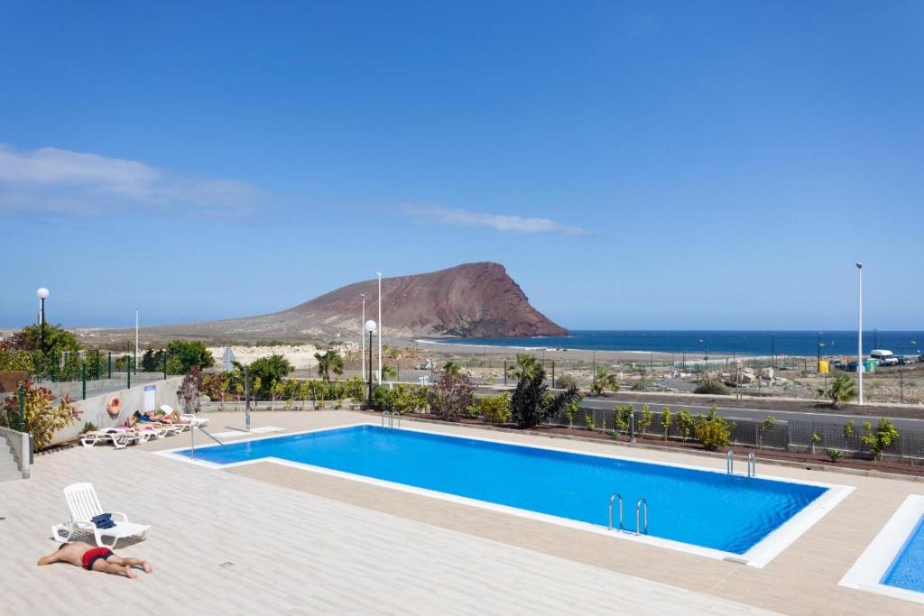a person laying on a towel next to a swimming pool at La Tejita, comfortable one-bedroom apartment in El Médano