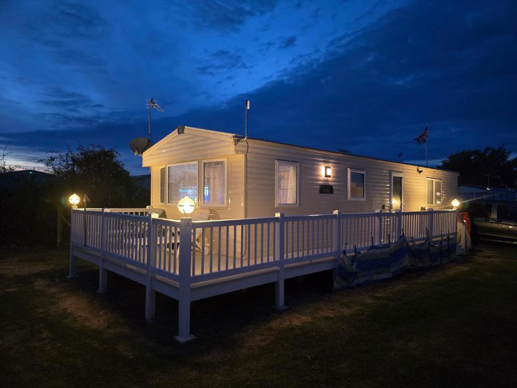 een klein wit huis met 's nachts verlichting bij 2 Bed Caravan With Decking in Saint Osyth
