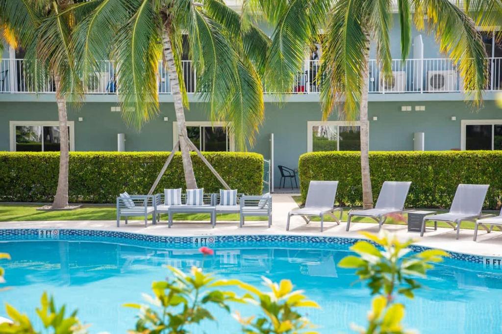 a pool with chaise lounge chairs and palm trees at Summertime Suites #49 in West Bay