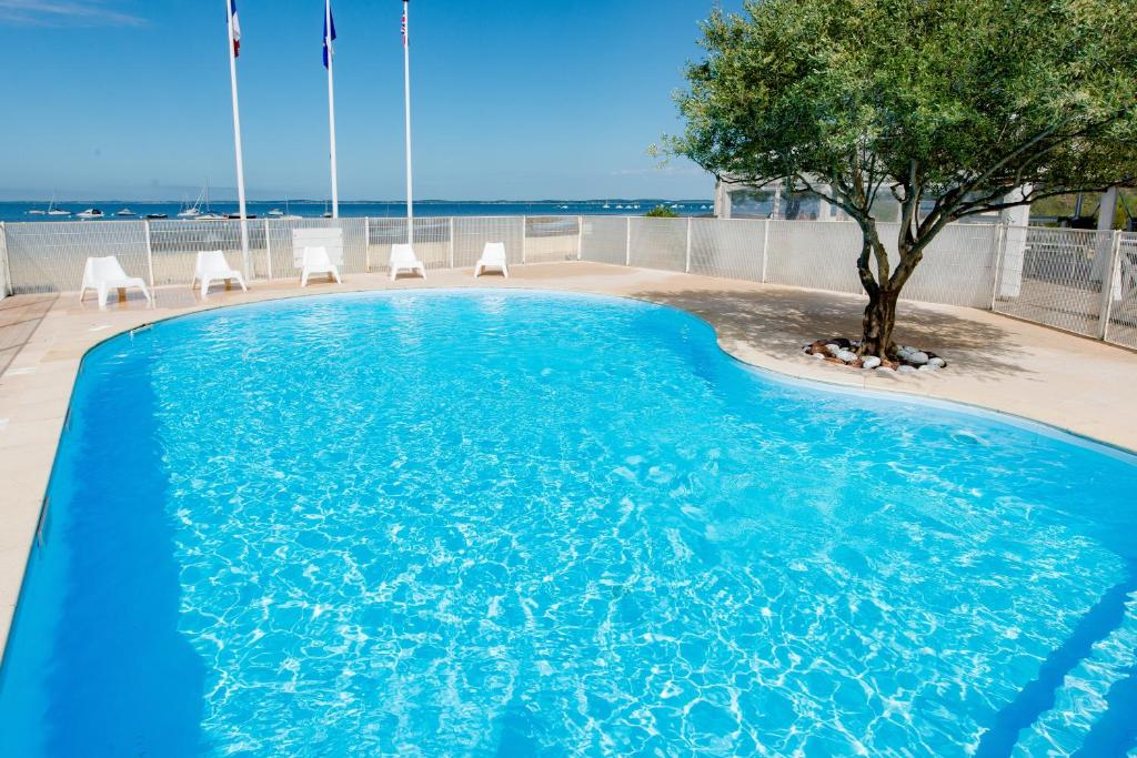 uma piscina com uma árvore e cadeiras em Hôtel L'Océane em Andernos-les-Bains