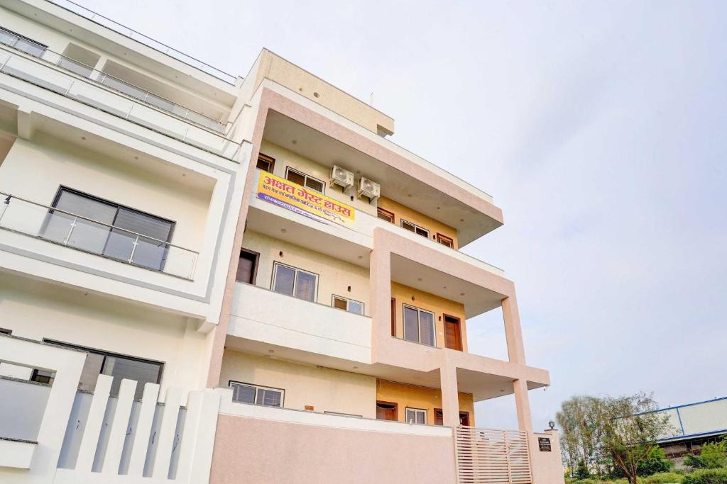 a tall white building with a yellow sign on it at Hotel O akshat guest house in Somarda Kauasot
