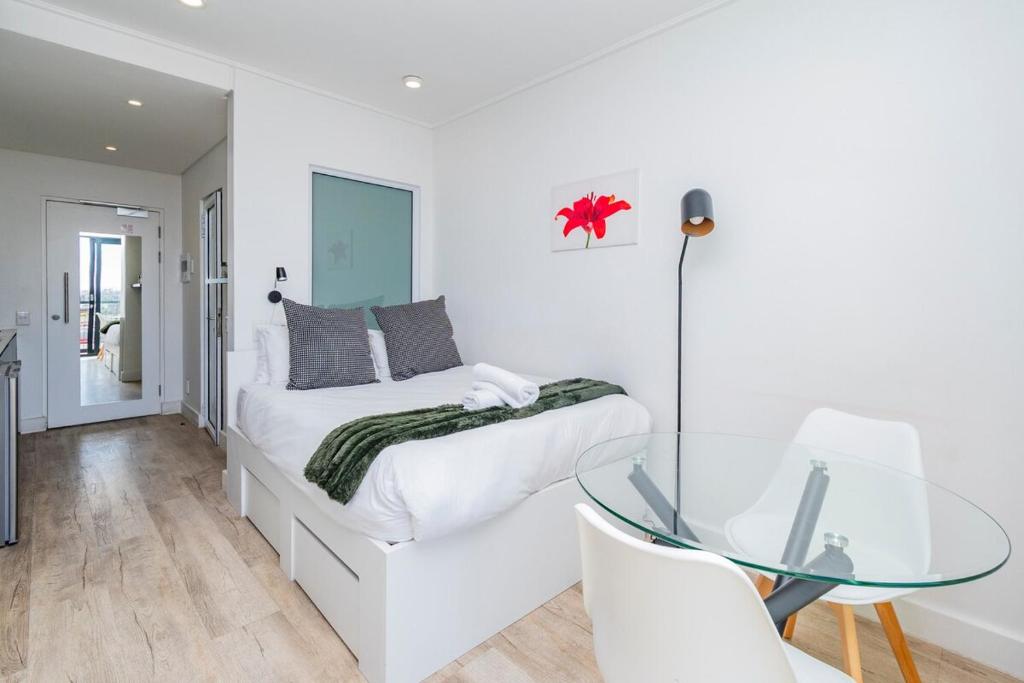 Dormitorio blanco con mesa de cristal y cama en Stylish Studio in One on Albert, en Hout Bay