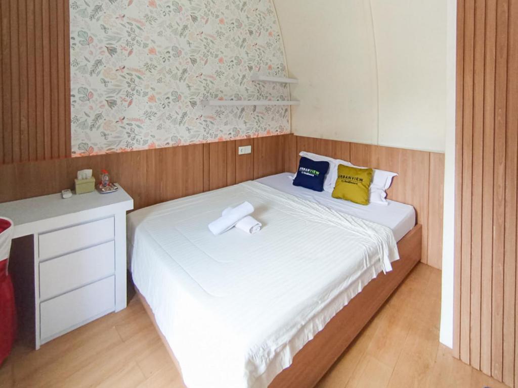 a small bedroom with a white bed with yellow and blue pillows at Urbanview Hotel Trisna Srabah in Kalangbret