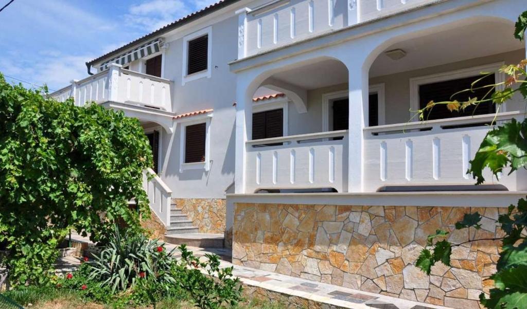 a white house with a porch and a stone wall at Apartments Kalsan in Novalja