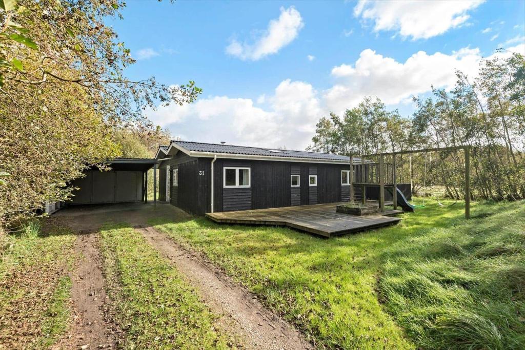 a black cabin in a field next to a dirt road at FAN049-Fano-Larses-Toft-31 in Fanø