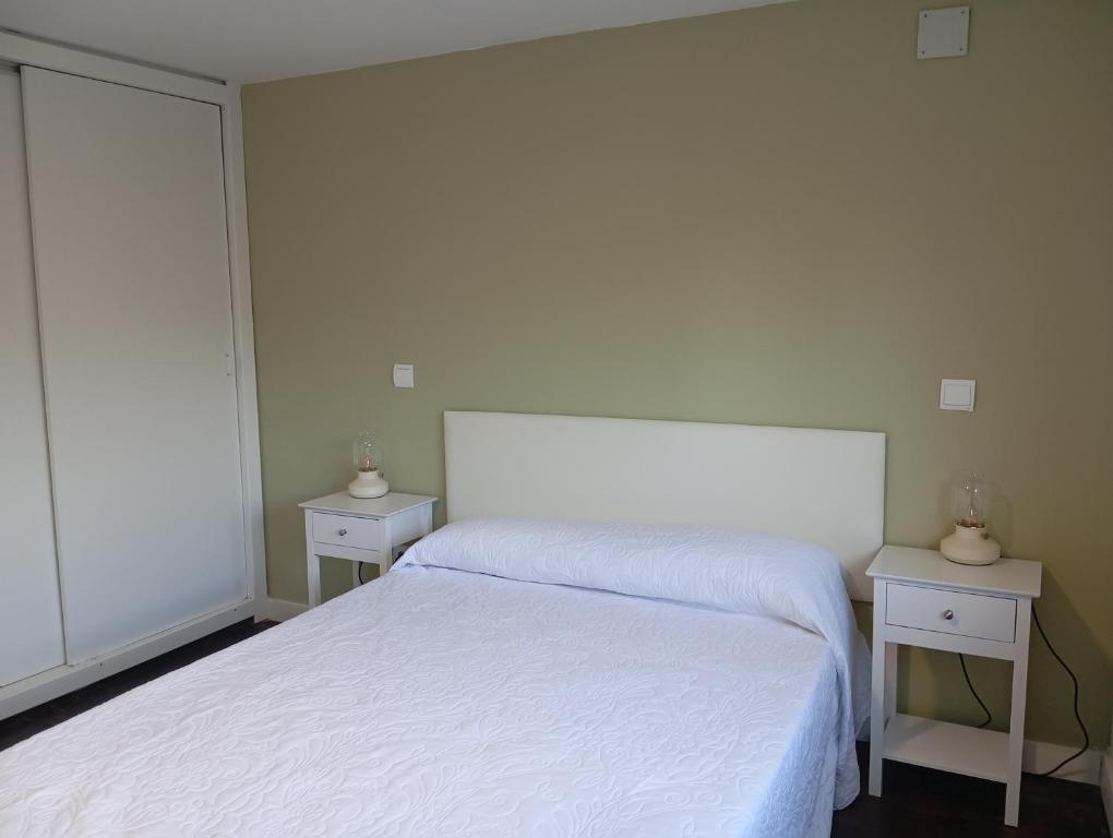 a white bedroom with two tables and a bed at La Casa de Pepe in Muros de Nalón
