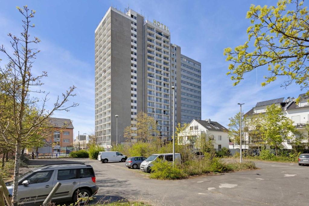 a tall building with cars parked in a parking lot at MONTAGO Monteur-Apartmenthaus Frankfurt Airport in Neu Isenburg
