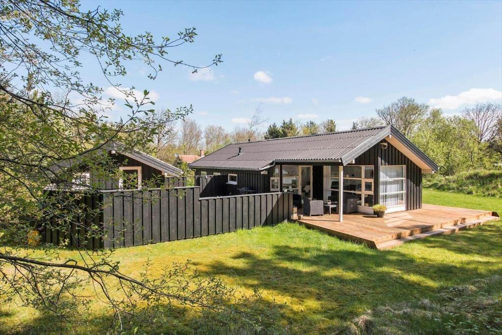 a black house with a wooden deck in a yard at BL1739-Blokhus-Bag-Hojen-47 in Blokhus