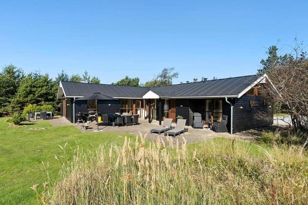 布洛克胡斯BL1718-Blokhus-Ronliensvej-16的田野里有一栋黑色的房子，有露台和椅子