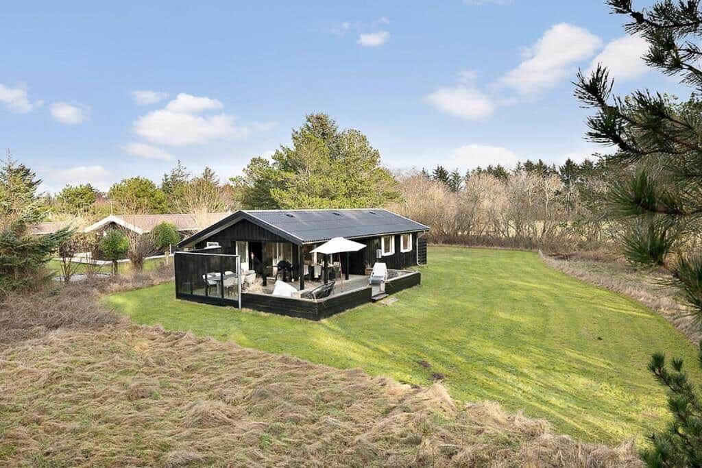 una casa nera su un campo erboso con alberi di BL1274-Blokhus-Raappenmark-30 a Blokhus
