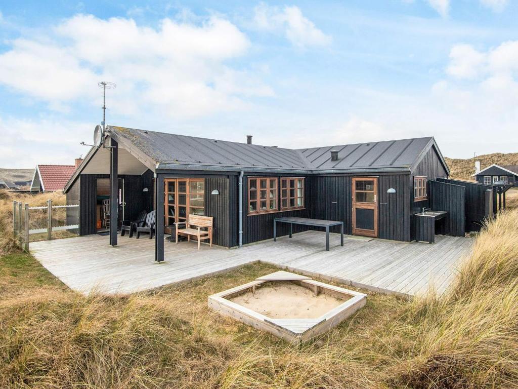 a black house with a wooden deck and a table at Cozy Retreat by the Sea - By Traum Ferienwohnungen in Hvide Sande