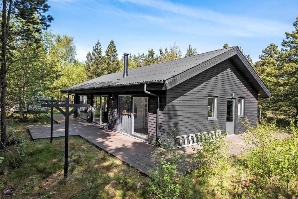una pequeña casa negra con terraza de madera en BL1266-Pandrup-Rodhusparken-58, en Pandrup
